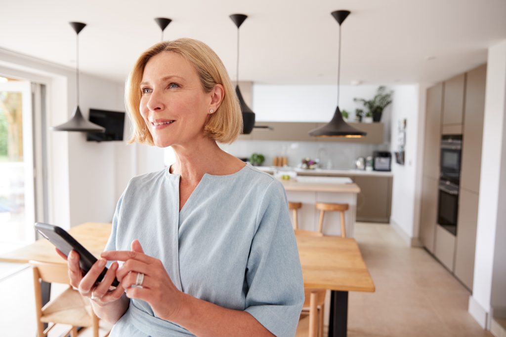 Mature Woman Using App On Mobile Phone To Control Central Heating Temperature In House